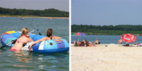 Links schwimmen zwei Personen auf Schlauchbooten in einem See, rechts entspannen sich Menschen unter Sonnenschirmen an einem Sandstrand, mit Bäumen im Hintergrund.
